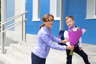 Annesi ve okul bahçesinde bir buket renkli çiçekle okul üniforması giyen birinci sınıf tatlı bir çocuk. Kutlama 1 Eylül 'de. Bilgi toplama günü. Seçici odak