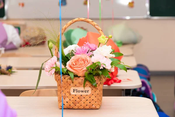 School class on September 1st without students. There is a wicker basket with flowers on the desk against the background of the school board. Selective focus. Close-up