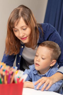 Yedi yaşında tatlı bir çocuk salgın sırasında annesiyle birlikte beyaz tahta bir masada ödev yapıyor. Seçici odaklanma. Yakın plan. Portre