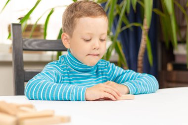 Evinde, beyaz bir tahta masada arka planda ışık penceresinin önünde Jenga oynayan yedi yaşında tatlı bir çocuk. Seçici odaklanma. Yakın plan. Portre