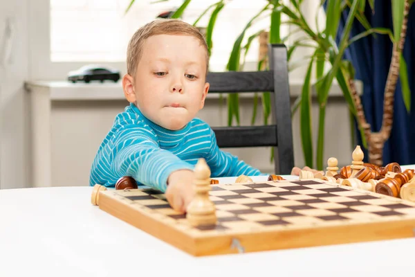 Evde beyaz tahta bir masada satranç oynayan yedi yaşında tatlı bir çocuk. Seçici odaklanma. Yakın plan. Portre