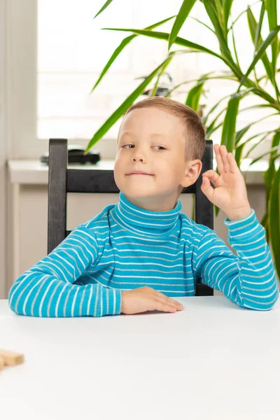 Een Schattige Zevenjarige Jongen Zit Thuis Aan Een Witte Houten — Stockfoto