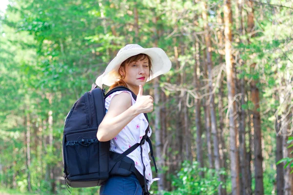 一个阳光灿烂的夏天 年轻的女游客背着背包 头戴草帽 站在绿树成荫的森林里 有选择的重点 — 图库照片