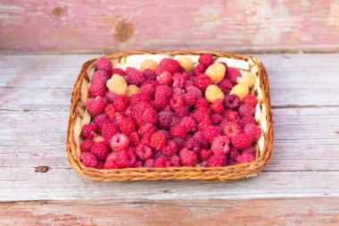 Ahşap bir arka planda sepetteki taze kokulu kırmızı ve sarı ahududular. Seçici odaklanma. Yakın plan.