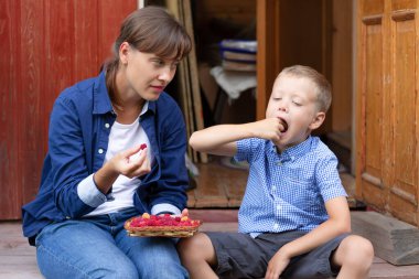 Altı yaşında bir çocuk annesiyle birlikte evin verandasındaki köyde taze kokulu ahududu yiyor. Seçici odaklanma. Portre