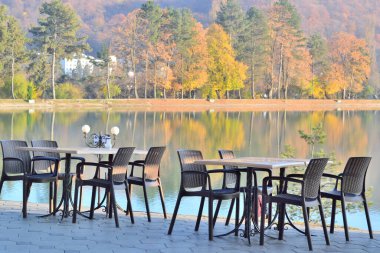 Gölün kıyısında turistler ve insanlar olmadan masalar ve sandalyeler duruyor.
