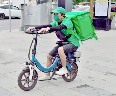 Yemek teslimatı için bir kurye bir kutuyla elektrikli bisiklet sürüyor.