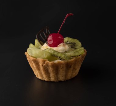 Kirazlı meyveli pasta, çikolata yaprağı, kivi kamaları ve siyah arka planda protein kremi.