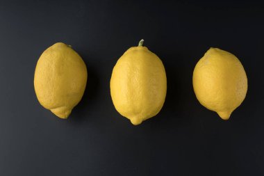 Üç koca limon, siyah bir arka planda, tek sıra halinde dizilmiş.