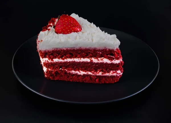 Piece of cake covered with protein cream and strawberries on a black plate and black background isolated — Zdjęcie stockowe