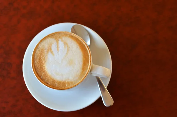 Cup of cappuccino with foam in a white porcelain mug with a spoon on a burgundy table — Fotografia de Stock