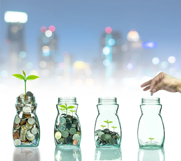 Mão colocando moedas de mistura e sementes em garrafa clara na foto cityscape desfocado fundo bokeh, conceito de crescimento de investimento de negócios — Fotografia de Stock