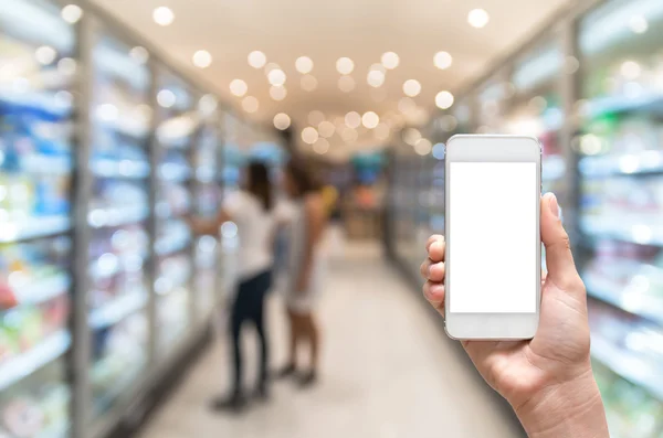 Mão feminina segurando telefone inteligente móvel no fundo de borrão do supermercado, conceito de negócio — Fotografia de Stock