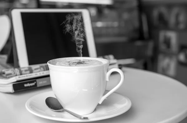 Coffee cup on the table in shop with tablet background — Stock Photo, Image