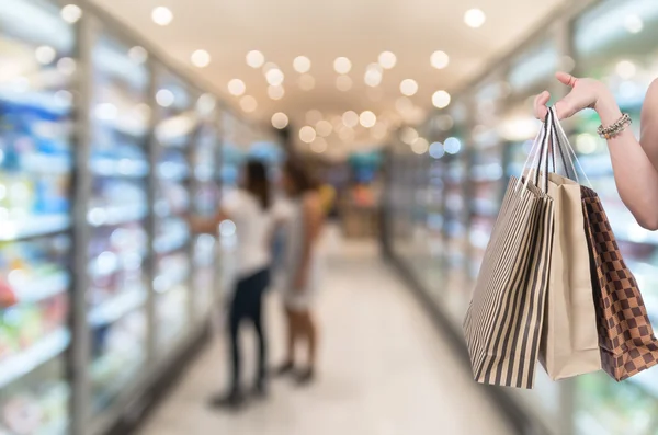 Sosteniendo bolsas de compras a mano en el fondo borroso del supermercado con bokeh, Varios Estante del producto —  Fotos de Stock