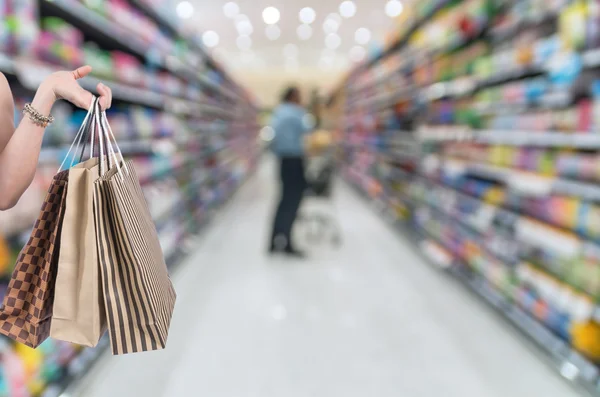 Sosteniendo bolsas de compras a mano en el fondo borroso del supermercado con bokeh, Varios Estante del producto —  Fotos de Stock