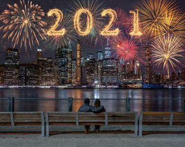 2021 'de arka tarafta oturan ve New York' un arka planına bakan çift üzerinde havai fişek renginde ışıltılı havai fişeklerle yazılmış, ABD şehir merkezi silueti, mutlu yıllar ve mutlu Noeller konsepti.