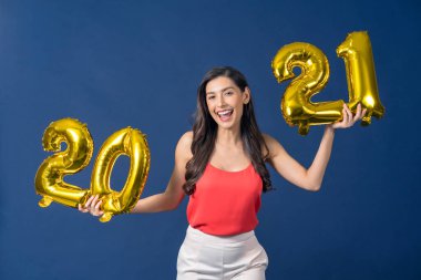 Mutlu Asyalı genç bir kadın elinde 2021 altın renkli balonlar tutuyor Mutlu Noeller ve mutlu yıllar mavi arka plan, bayram etkinliği için kutlama ve süsleme üzerine