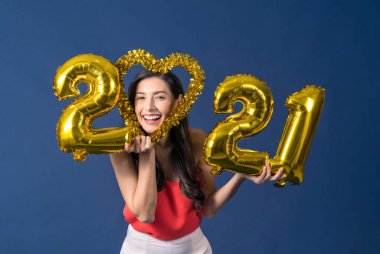 Mutlu Asyalı genç bir kadın elinde 2021 altın renkli balonlar tutuyor Mutlu Noeller ve mutlu yıllar mavi arka plan, bayram etkinliği için kutlama ve süsleme üzerine