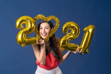 Mutlu Asyalı genç bir kadın elinde 2021 altın renkli balonlar tutuyor Mutlu Noeller ve mutlu yıllar mavi arka plan, bayram etkinliği için kutlama ve süsleme üzerine