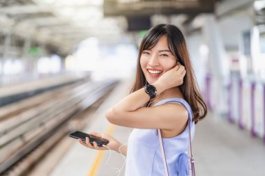 Genç Asyalı kadın yolcu metroda, Japonca, Çince, Kore yaşam tarzı ve günlük yaşam, banliyö ve ulaşım kavramında seyahat ederken akıllı cep telefonuyla müzik dinliyor.