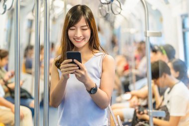 Genç Asyalı kadın yolcu metroda seyahat ederken, metroda, Japonca, Çince, Kore yaşam tarzı ve günlük yaşamında, banliyö ve ulaşım kavramında sosyal ağı akıllı cep telefonuyla kullanıyor.