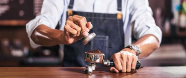 Kafede müşterilerin siparişi için portafilteri dolduran ve kahve, kahve, kahve ya da kapuçino hazırlayan Asyalı baristanın bayrağı, küçük işletme sahibi ve kahve dükkanı kavramının başlangıcı.