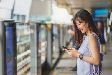 Genç Asyalı kadın yolcu metroda seyahat ederken, metroda, Japonca, Çince, Kore yaşam tarzı ve günlük yaşamında, banliyö ve ulaşım kavramında sosyal ağı akıllı cep telefonuyla kullanıyor.
