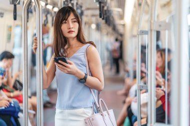 Genç Asyalı kadın yolcu metroda seyahat ederken, metroda, Japonca, Çince, Kore yaşam tarzı ve günlük yaşamında, banliyö ve ulaşım kavramında sosyal ağı akıllı cep telefonuyla kullanıyor.