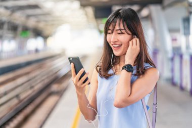 Genç Asyalı kadın yolcu metroda, Japonca, Çince, Kore yaşam tarzı ve günlük yaşam, banliyö ve ulaşım kavramında seyahat ederken akıllı cep telefonuyla müzik dinliyor.
