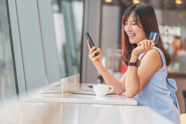 現代のコーヒーショップでオンラインショッピングのための携帯電話とクレジットカードを使用してアジアの女性 テクノロジーマネーウォレットとオンライン決済の概念 クレジットカードのモックアップ ロイヤリティフリーのストック画像