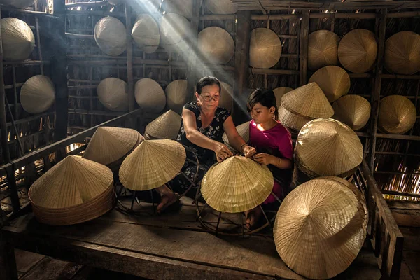 Vietnamese Old woman craftsman teaching the grandchild making the traditional vietnam hat in the old traditional house in Ap Thoi Phuoc village, Hochiminh city, Vietnam, traditional artist concept