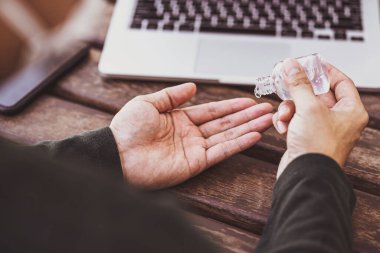 Asyalı bir adamın el dezenfektanı kullanırken, teknoloji laptopuyla çalışmadan önce alkol jeli pompalarken, Covid-19 salgını, sosyal mesafe ve sorumluluk konseptiyle evden çalışırken,