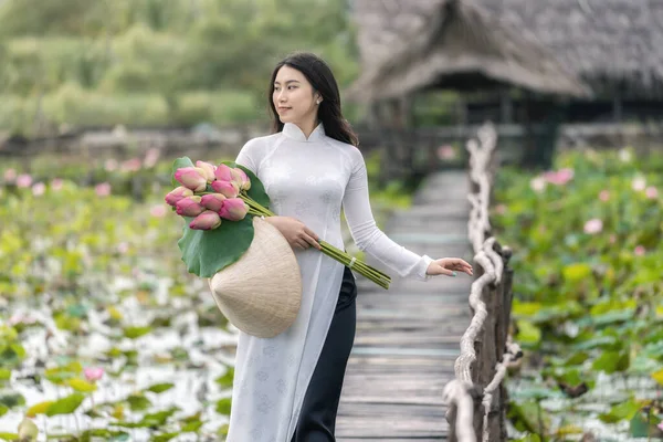 大きな蓮の湖 ベトナム アジアや東南アジアの旅行の概念で木製の橋の上にピンクの蓮の散歩を保持伝統的なベトナムの帽子と美しいベトナムの女性の肖像画 — ストック写真