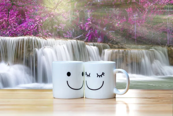 Zwei glückliche Tassen auf Holztisch mit schönem Wasserfall im — Stockfoto