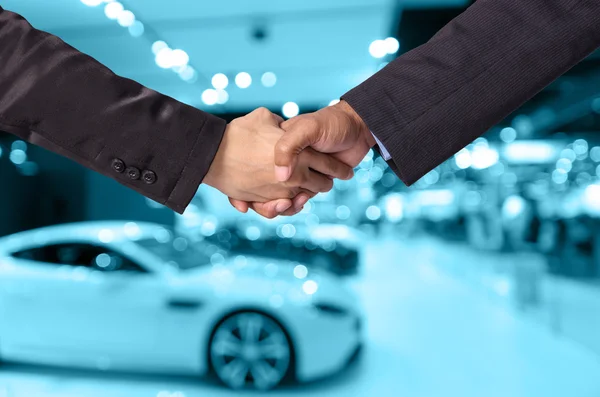 Hand shake between a businessman and a businesswoman on abstract blurred photo of motor show background — Stock Photo, Image