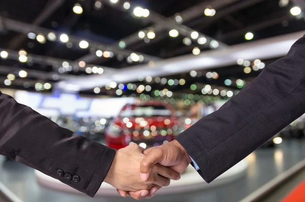 Hand shake between a businessman and a businesswoman on abstract blurred photo of motor show background — Stock Photo, Image