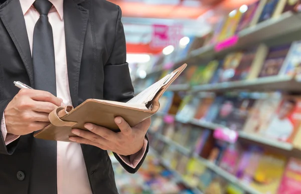 Geschäftsmann schreibt das Notizbuch auf abstrakten verschwommenen Foto des Buchhandels Hintergrund, verwischen Farbton — Stockfoto