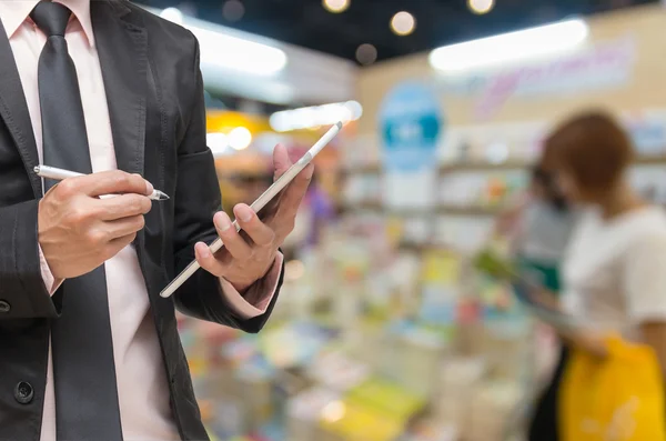 Businessman using the tablet on on Abstract blurred photo of book store with people background — Stock Photo, Image