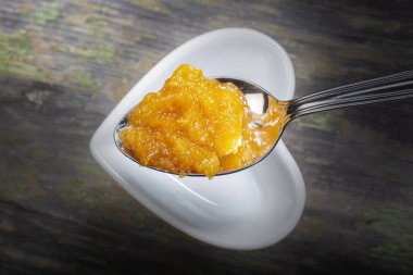 Bir kaşık taze portakal reçeli. Altında Tahta Arkaplan 'da Beyaz Kalp Biçimli Kâse var.. 