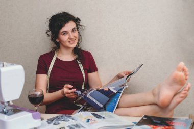 Mutlu ve çekici genç bayan terzi stüdyoda dikiş makinesine oturup dikiş dikiyor.