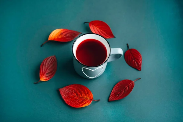 Autumn leaves and a cup of red Hibiscus herbal tea on green background. — Stock Photo, Image