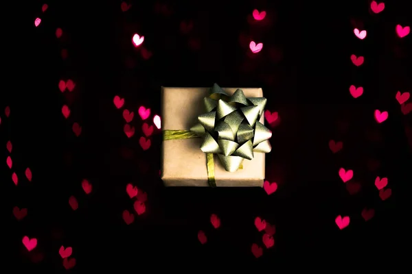Pequeña caja de regalo artesanal sobre fondo negro con corazones rojos bokeh. — Foto de Stock