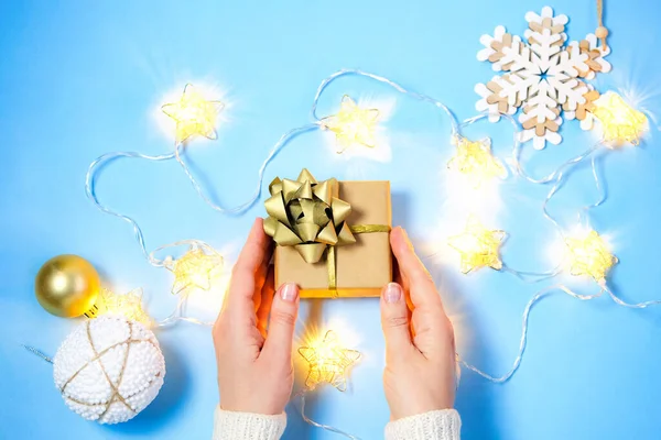 Manos femeninas tomando regalo colorido con cintas blancas sobre fondo azul claro — Foto de Stock