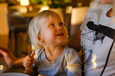 Genç anne, küçük çocuğuyla kapalı bir kafede pizza yerken dinleniyor..