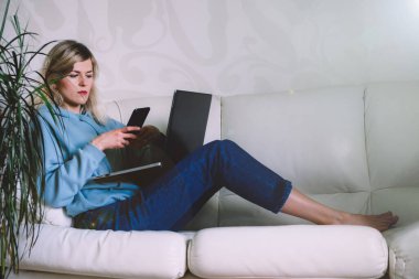 İş kadını kanepede otururken cep telefonuna bakıyor.