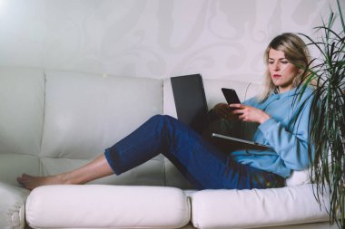 İş kadını kanepede otururken cep telefonuna bakıyor.