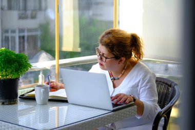 Evde çalışan olgun bir kadın balkonda oturuyor.