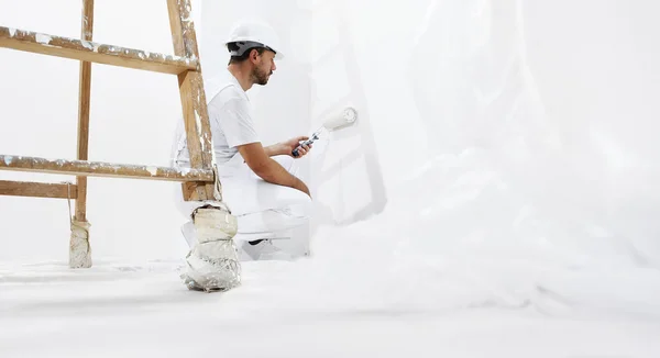 Peintre homme au travail avec un rouleau de peinture sur le mur — Photo