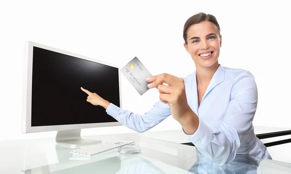 Mujer sonriente con tarjeta de crédito en la oficina en el escritorio frente a la computadora apuntando a la pantalla — Foto de Stock